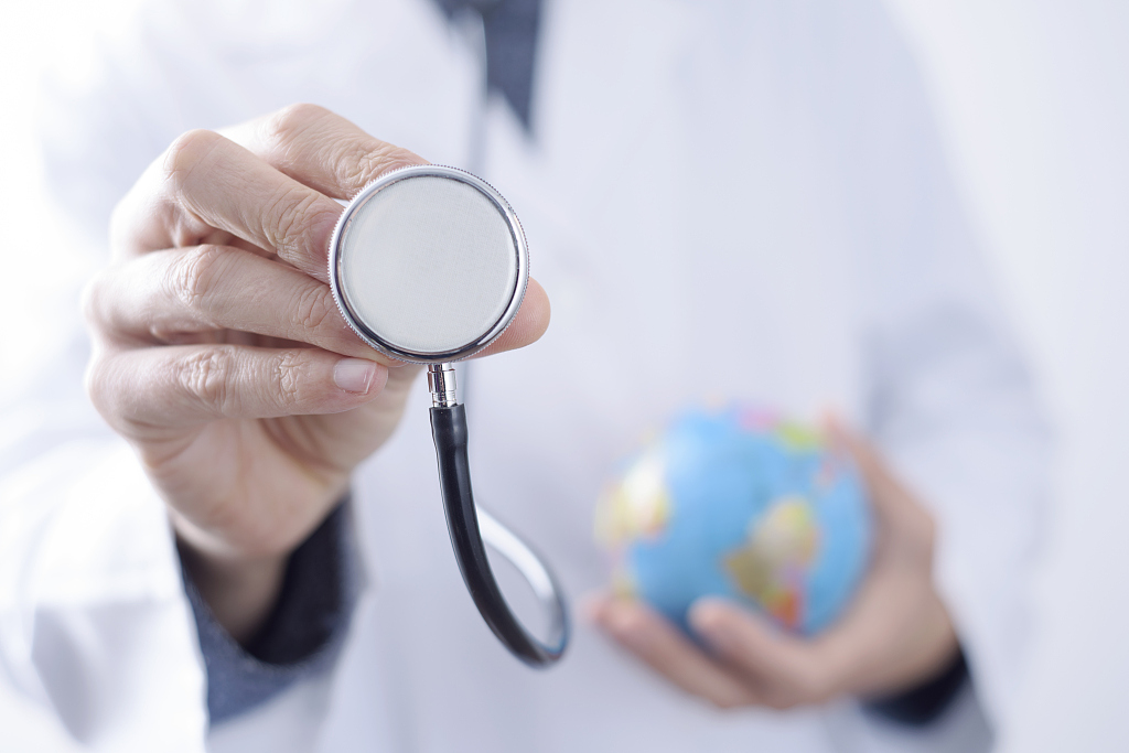 closeup of a young caucasian doctor man with a world globe in one hand and a stethoscope in the other hand